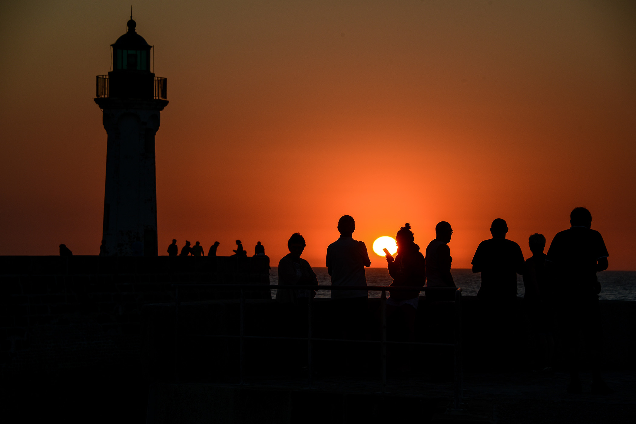 Silhouettes sur la jetée de Saint-Valery-en-Caux au coucher de soleil, avec le phare en contre-jour