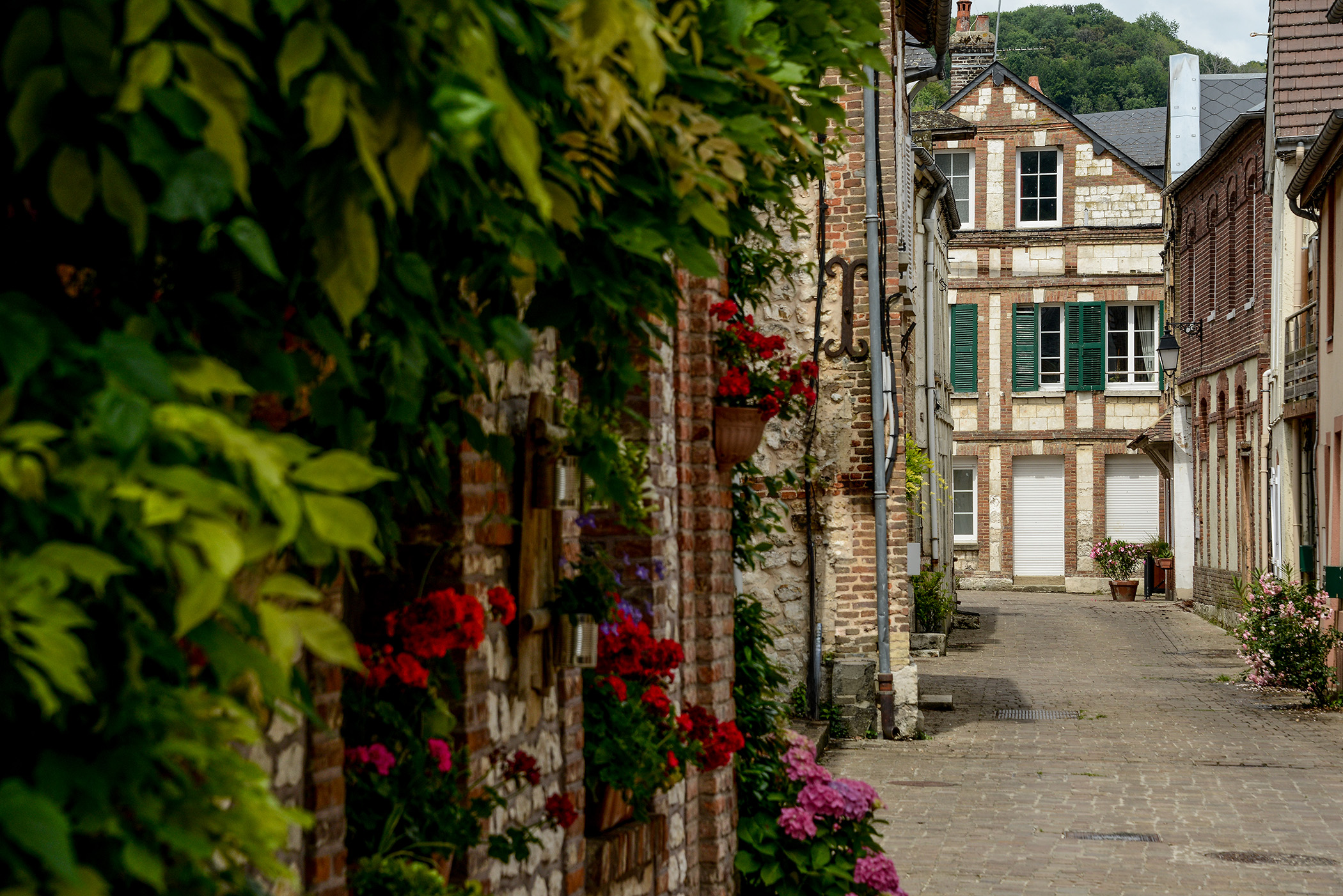 Ruelle fleurie avec maisons en brique et pierre dans un village de la vallée de la Seine en Normandie